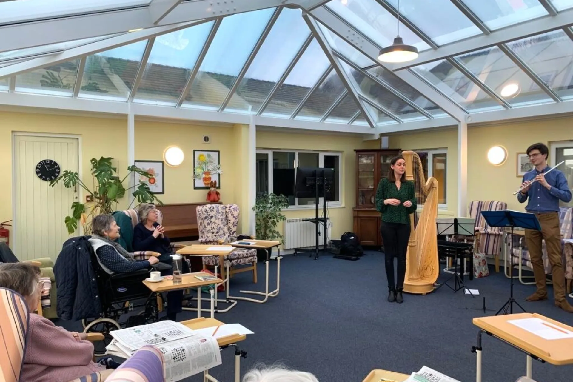 A flautist and harpist playing for a group of elderly people in a care home