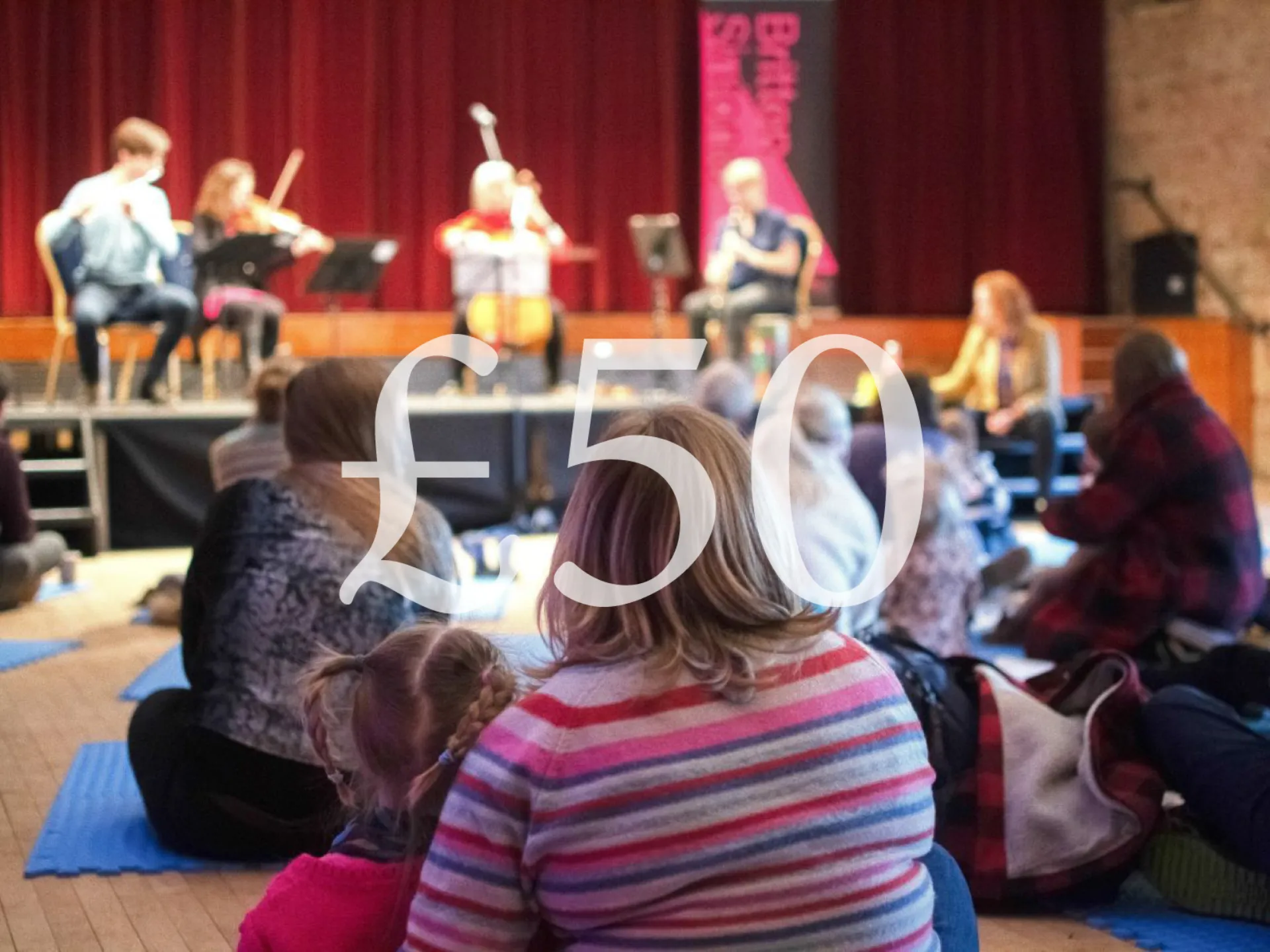 Children sit on a hall floor watching musicians perform on stage